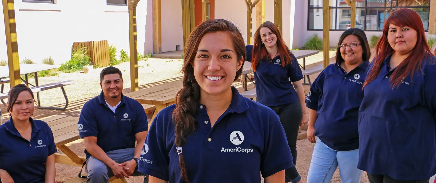 Six young adults in AmeriCorps branding shirts standing under a gazebo and sitting at picnic tables