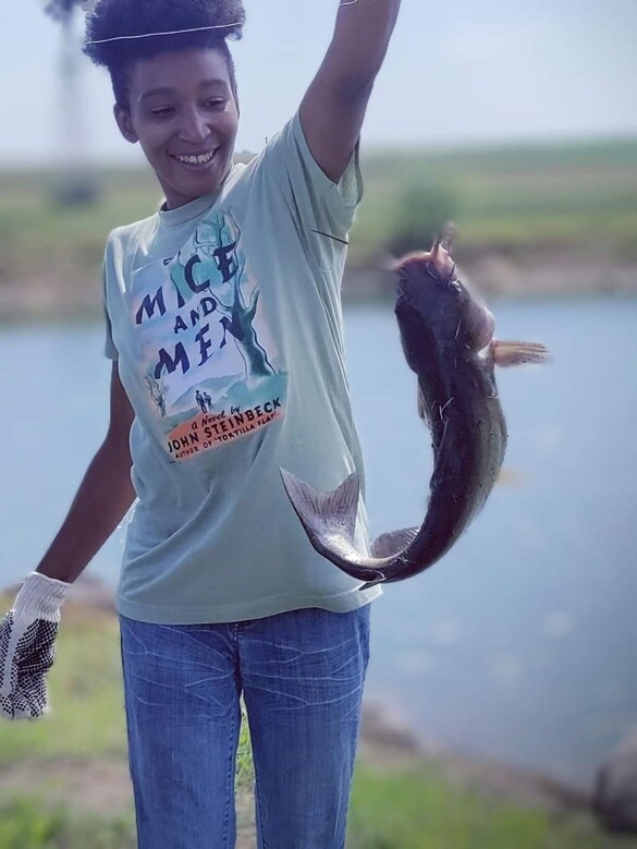 A young woman in front of a pond holding a fish
